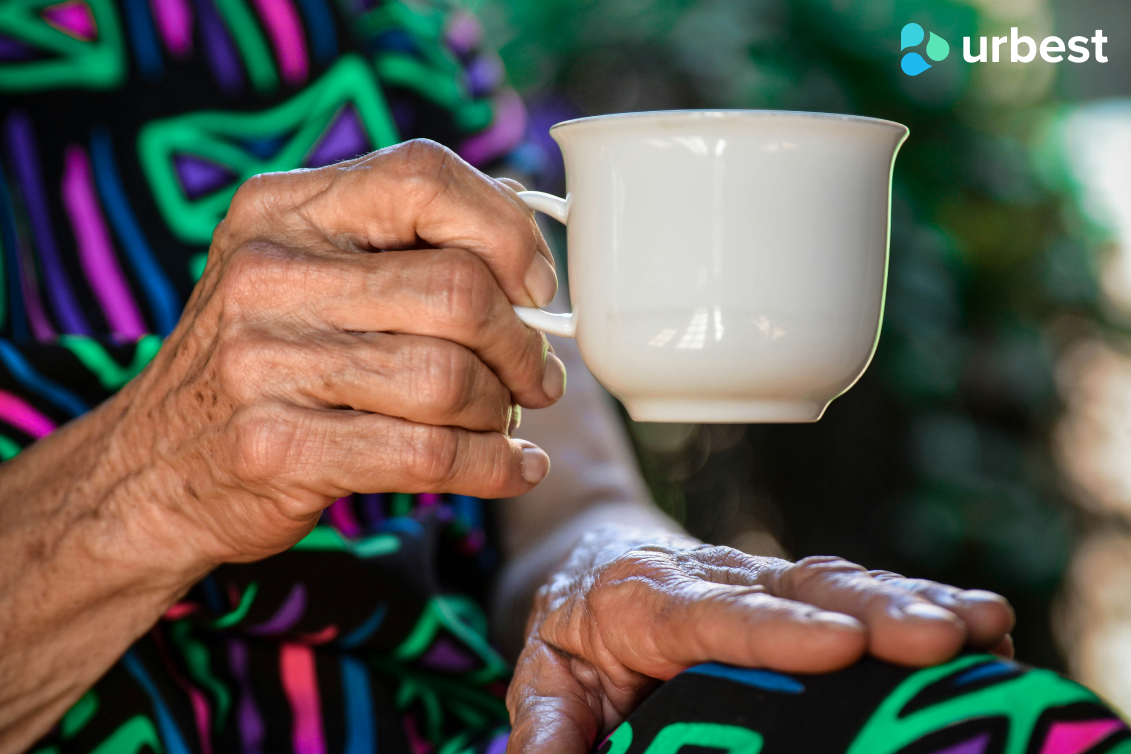 Elderly person's hand in a colorful printed dress holding a white cup. Picture by Claudia Love